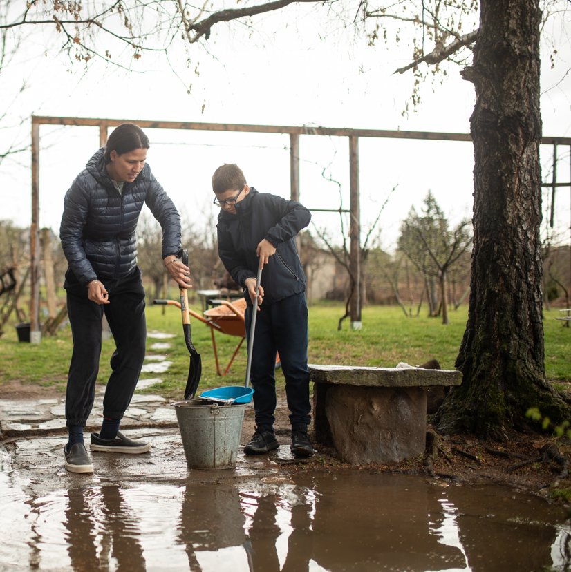 A mother helping her son clean up mud into a bucket